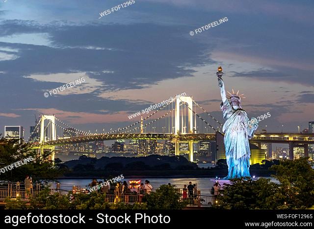 Japan, Kanto Region, Tokyo, Replica of Statue of Liberty and illuminated Rainbow Bridge at dusk