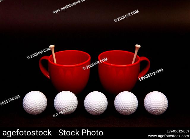 White golf balls and red cups of tea on the black table. White golf ball in front of a black background. Breakfast composition