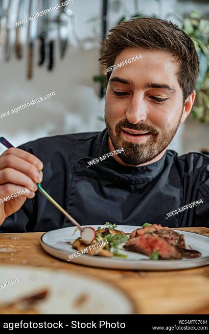 Smiling chef arranging cooked meat and vegetables in plate while standing in kitchen