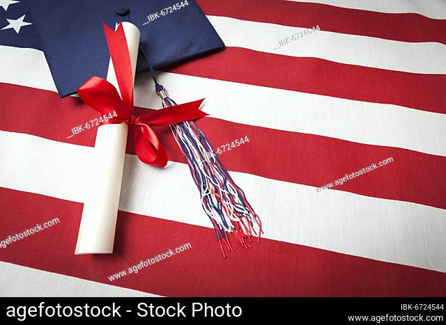 Graduation cap with tassel and red ribbon wrapped diploma resting on american flag