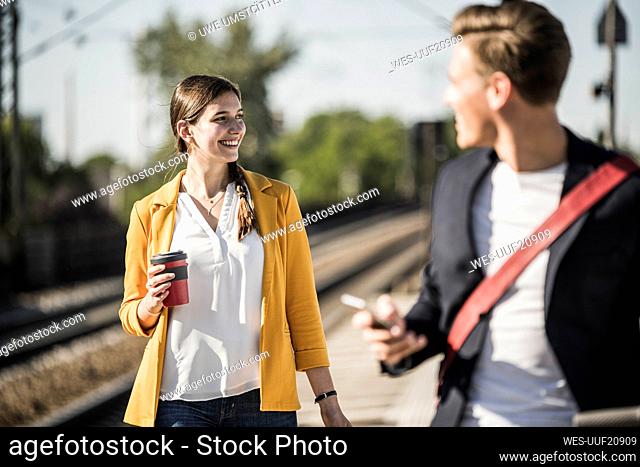 Smiling woman with reusable coffee mug looking away while walking at railroad station platform