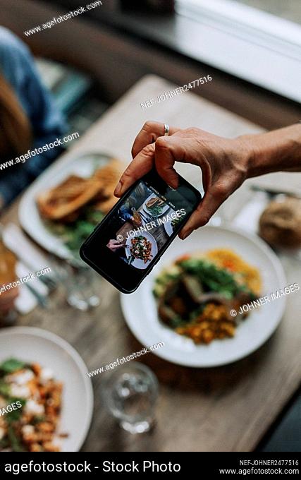 Hand with cell phone photographing food on table
