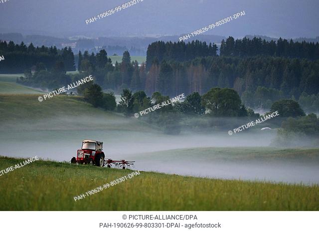 26 June 2019, Bavaria, Bernbeuren: A tractor stands on a field in the foothills of the Alps covered in morning fog. Photo: Karl-Josef Hildenbrand/dpa