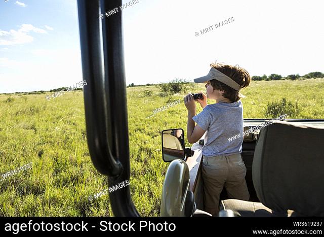A six year old boy with binoculars in a safari vehicle