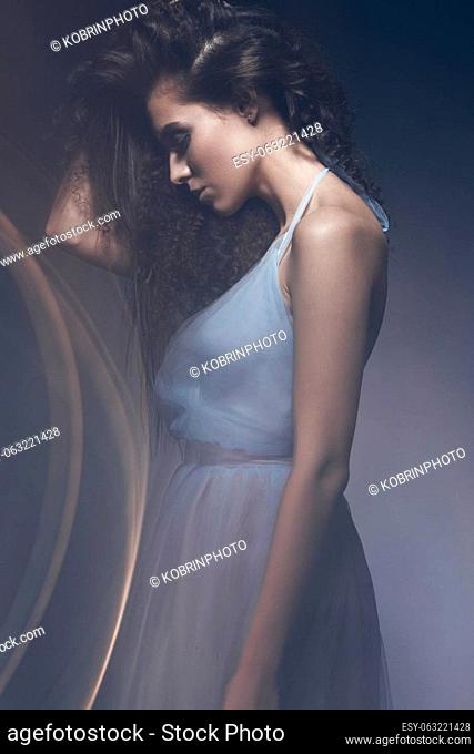 Beautiful girl in a light blue dress and long hair in a fashionable image. Beauty fashion style. Picture taken in the studio with mixed light