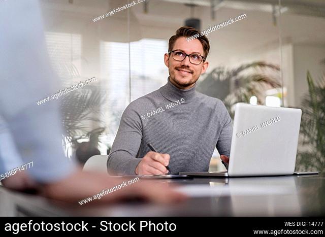Smiling businessman looking at male colleague while discussing in office