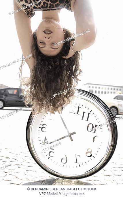 young emotional woman upside down with clock at street in city Berlin, Germany