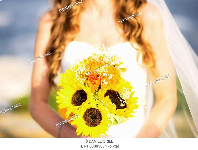 Mid section of bride holding sunflower bouquet