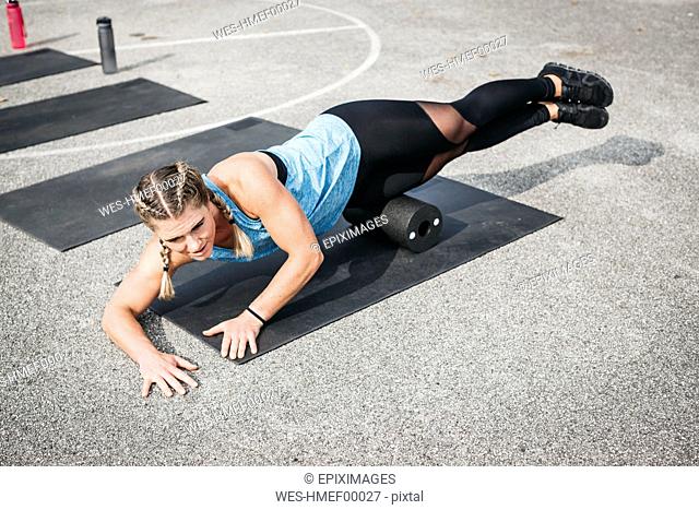 Woman doing workout exercise with fascia roll outdoors