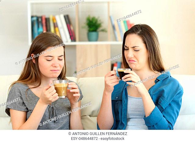Two friends drinking coffee with bad flavour sititng on a couch in the living room at home