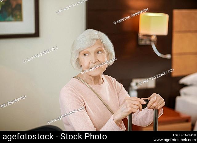 In a hotel. Good-looking senior woman sitting with a suitcase in a hotel room