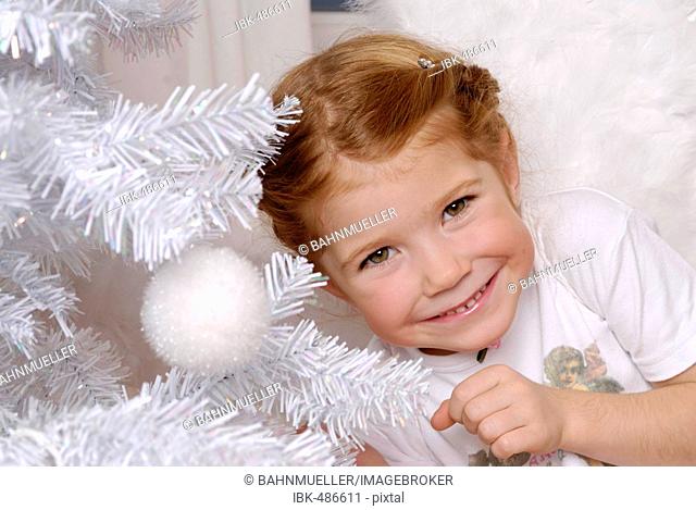 Child decorates a white christmas tree