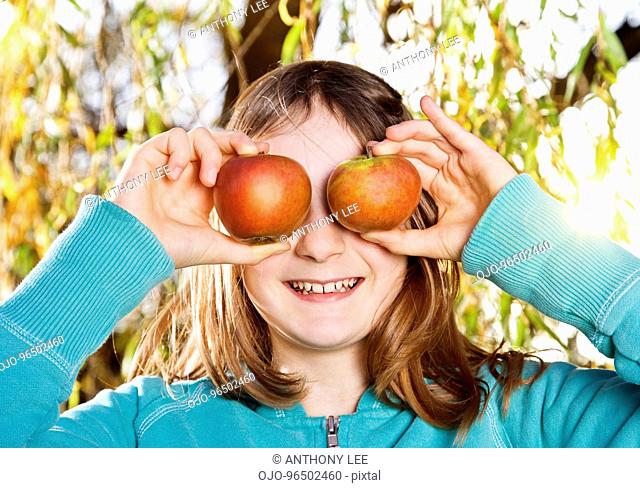 Girl holding apples over eyes
