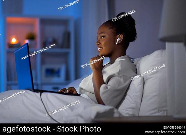 woman with laptop and earphones in bed at night