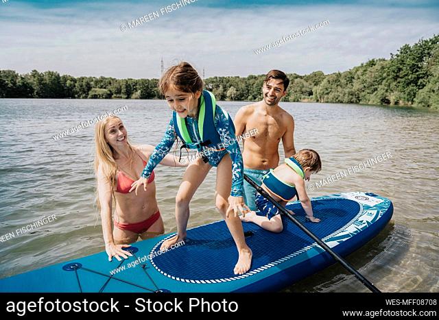 Siblings on paddleboard floating over lake by parents