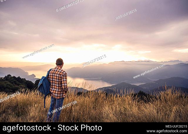 Mature man with backpack standing on mountain at sunset