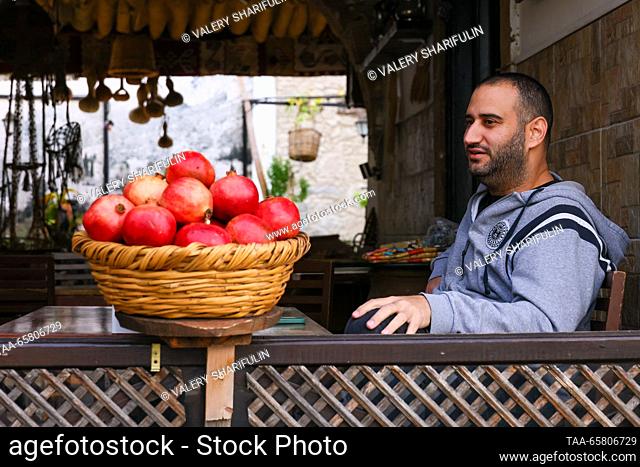 CYPRUS, KYRENIA - DECEMBER 15, 2023: A man sits next to a basket of pomegranates. The Turkish Republic of Northern Cyprus is a de facto state declared...