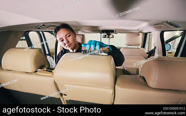 Vehicle cleaning - caucasian young woman is washing armchair of a luxury car with a brush, close up