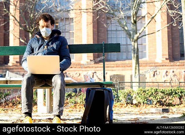 Man wearing protective face mask using laptop in public park