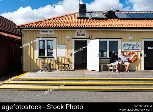 Oregrund, Uppland / Sweden - 30 07 2019: Facade and two elderly people sitting in front of an old harbor office or hamnkontoret for border control