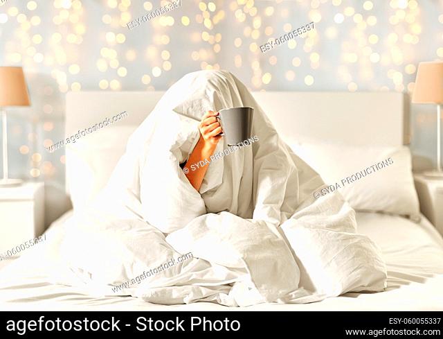 woman with coffee sitting under blanket in bed
