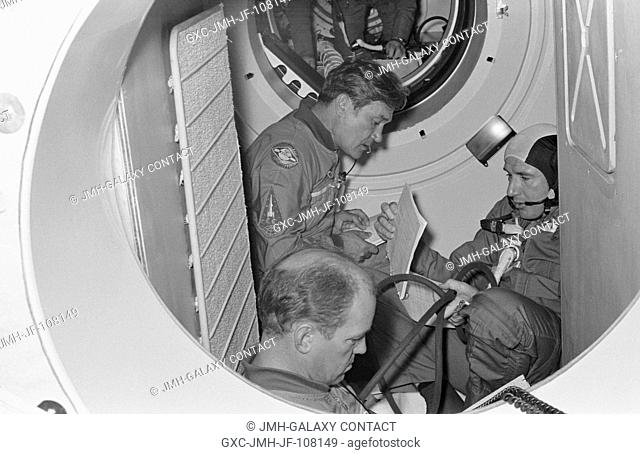 Three crewmen of the Apollo-Soyuz Test Project are seated in a Soviet Soyuz spacecraft orbital module mock-up in Building 35 during ASTP simulation training at...