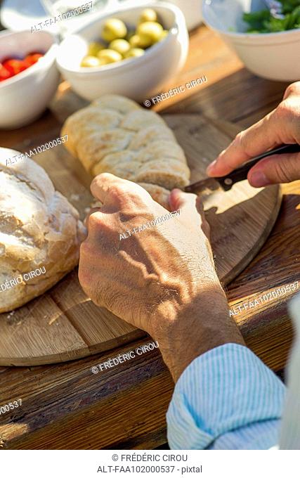 Man's hands cutting fresh loaf of bread outdoors