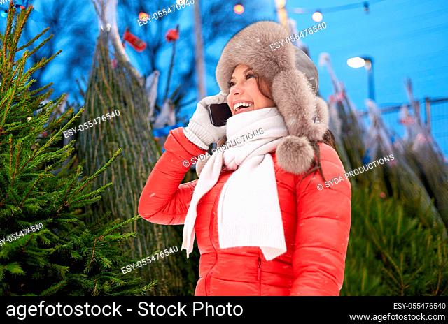 woman calling on smartphone over christmas trees