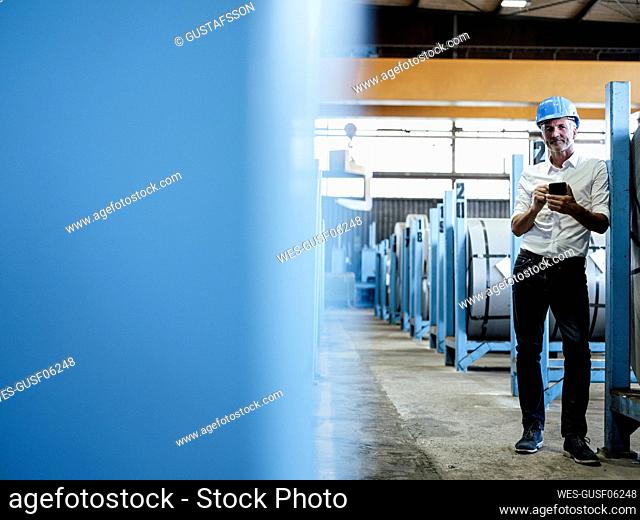 Male engineer with mobile phone standing at distribution warehouse