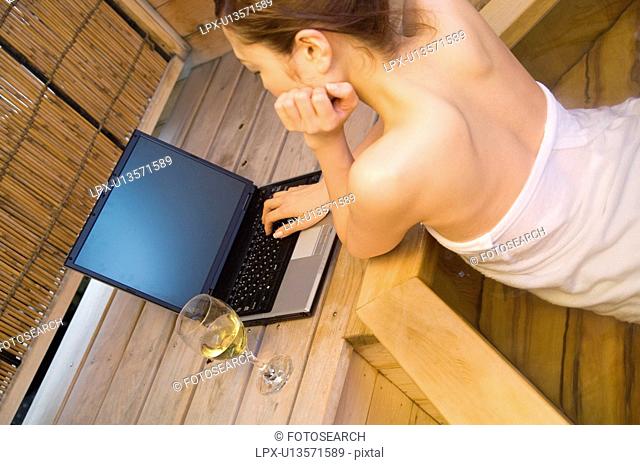 Woman using her laptop and drinking wine in a hot tub