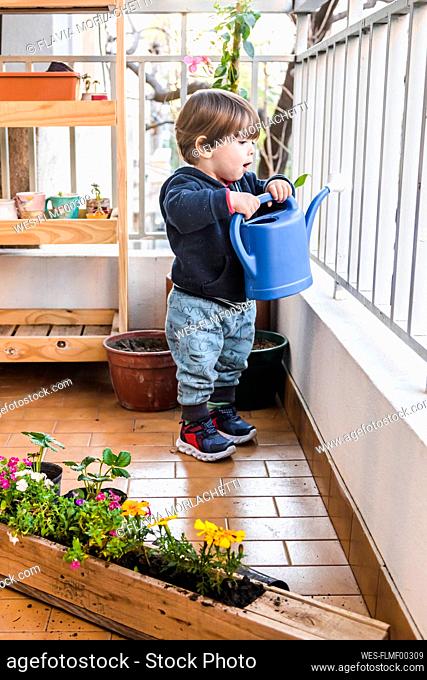 Cute boy holding watering can while standing by railing at balcony