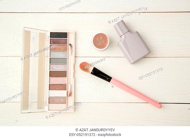 grey perfume bottle, highlighter, eye shadow and brush on light wooden background. flat lay