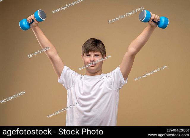Waist-up portrait of a boy working out with a pair of hand weights in front of the camera