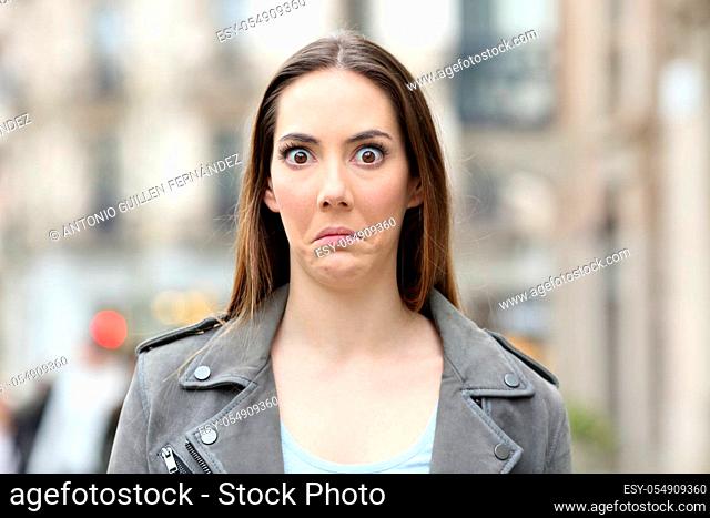 Front view portrait of a shocked young woman looking perplezed at camera on city street