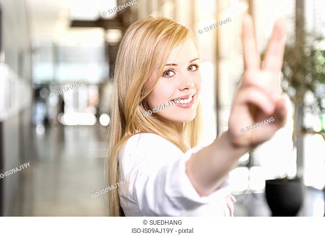 Portrait of confident young businesswoman making victory sign with hand