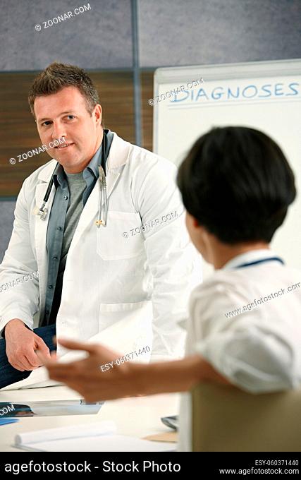 Two medical doctors chatting in doctor's room, smiling