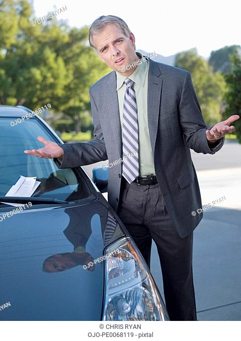 Frustrated businessman shrugging at parking ticket on windshield