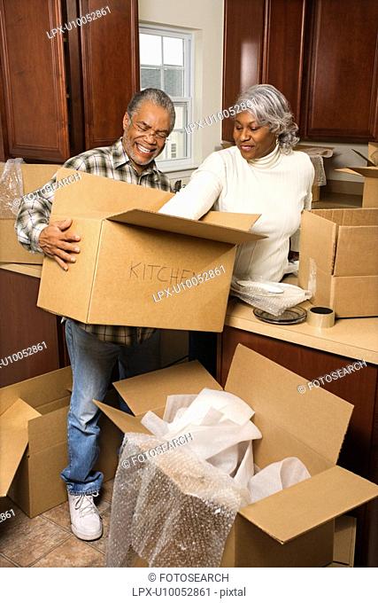 Portrait of middle-aged African-American couple packing moving boxes in kitchen