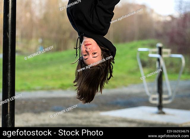 White teenage girl with brown hair hanging upside down like a bat on a climbing frame