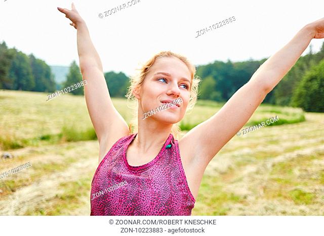 Junge Frau macht eine Yoga Übung in der Natur und streckt die Arme