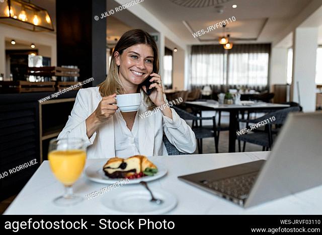 Smiling businesswoman holding coffee cup talking on mobile phone at restaurant
