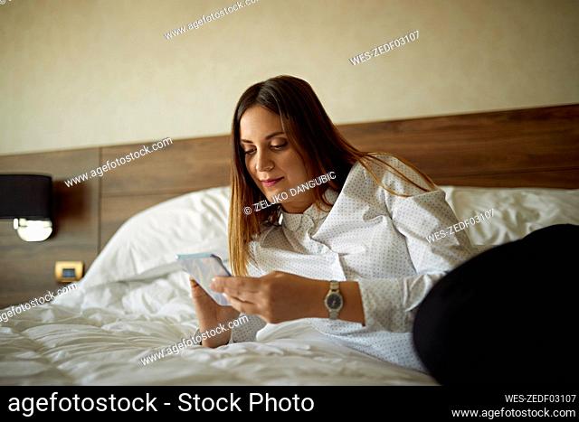 Businesswoman lying on bed in hotel room using cell phone