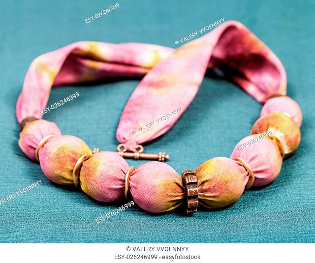 textile necklace from pink and yellow painted silk balls and copper rings on green background