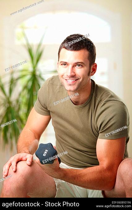 Muscular man doing biceps exercise at home with hand barbell, smiling