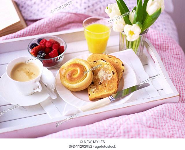 A breakfast tray with a cup of coffee, bread and toast, berries and fresh flowers