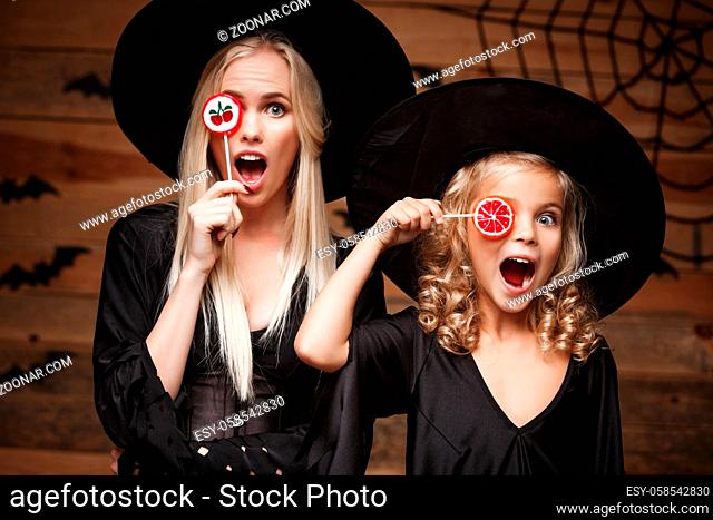 Halloween Concept: beautiful caucasian mother and her daughter in witch costumes celebrating Halloween with Halloween candy and sweet over bats and spider web...