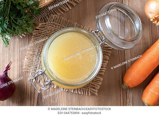 Chicken bone broth in a glass jar with fresh vegetables, top view