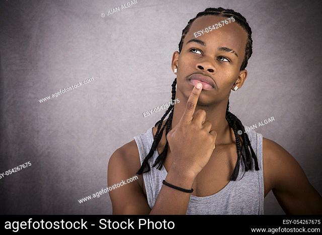 Young African-American man feeling thoughtful and touching lips on gray background