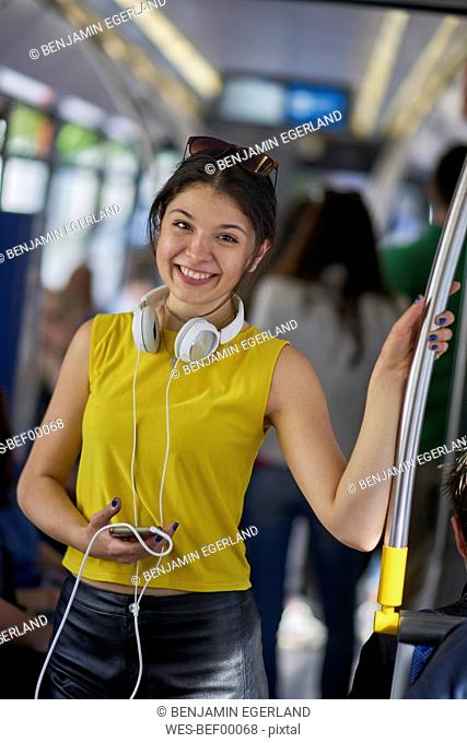 Portrait of smiling young woman with cell phone and headphones in underground train
