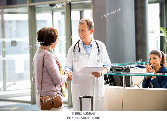 Male doctor shaking hands with his patient at hospital reception desk